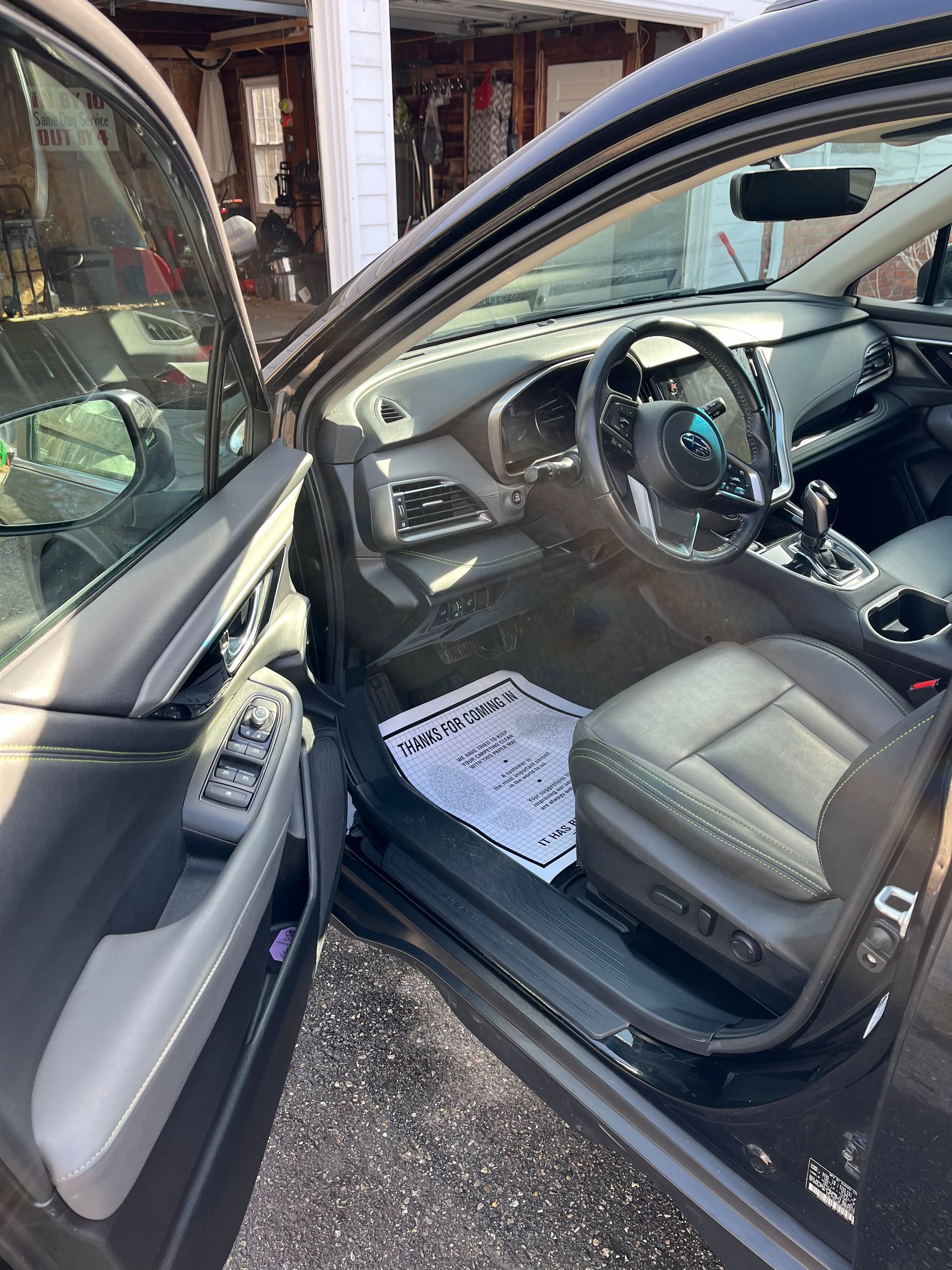 Open car door revealing a black leather driver’s seat and steering wheel, with papers on the floor mat.