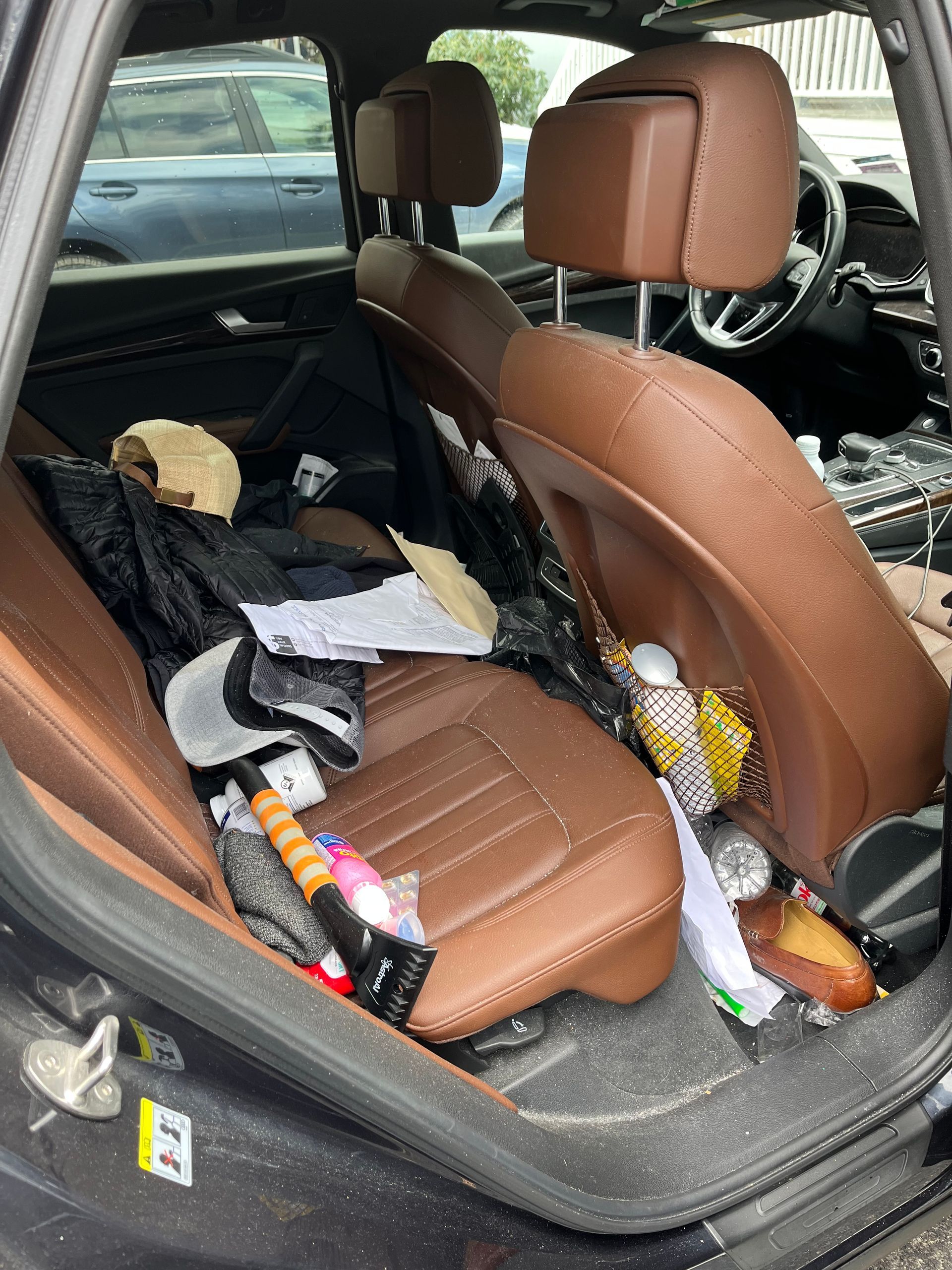 Messy car back seat with clothes, bottles, and trash scattered across brown seats