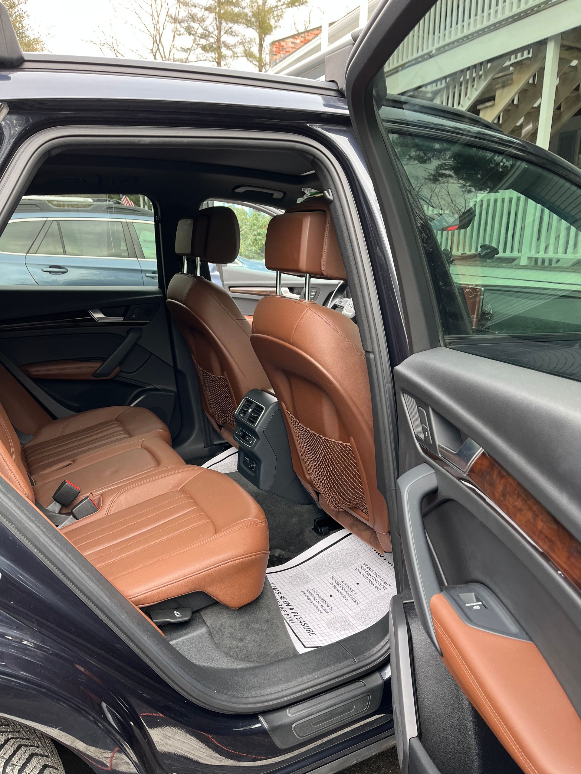 Open car door showing tan leather back seat and interior with black trim and floor mat