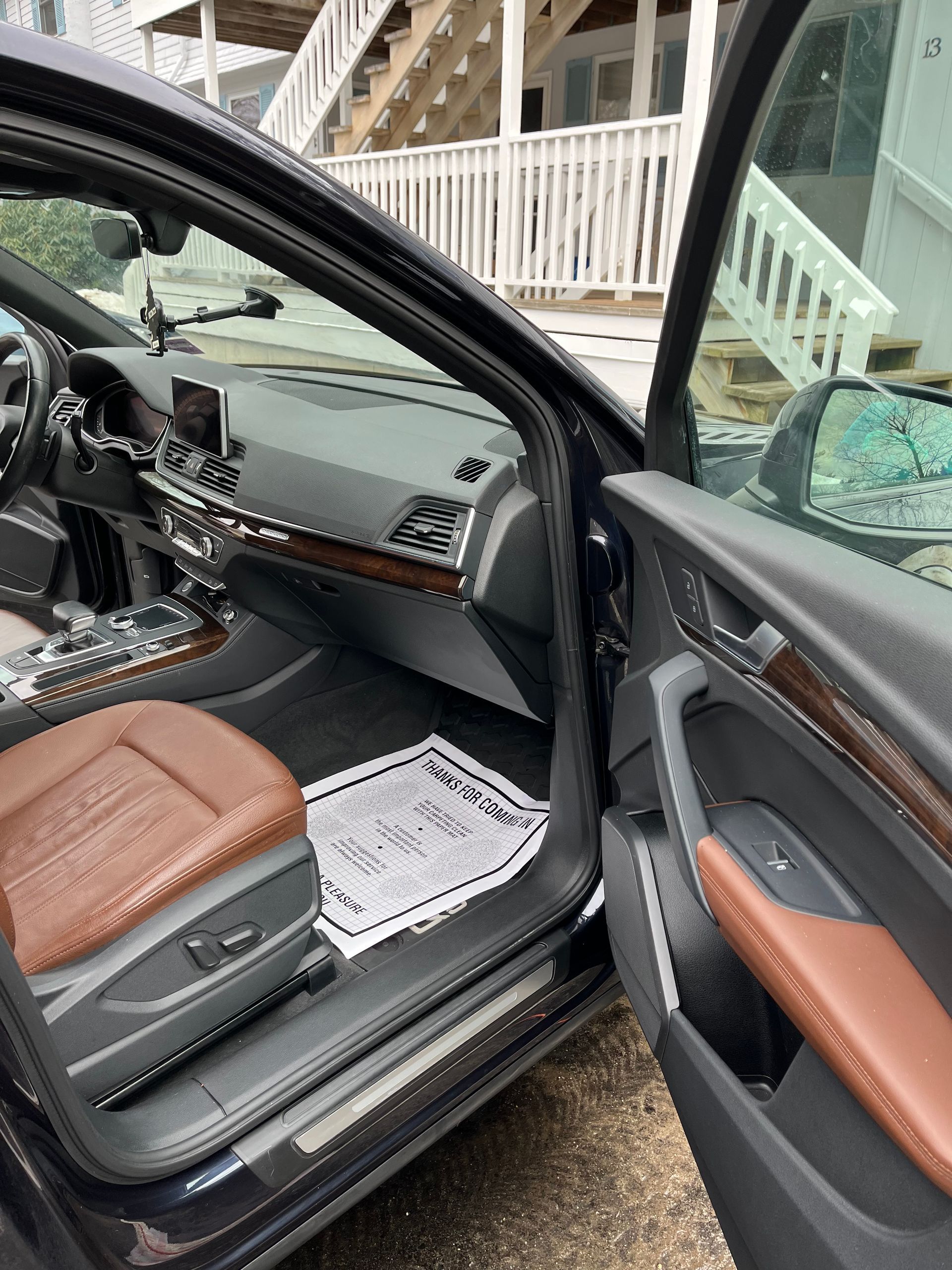 Open car door showing black and brown leather interior with dashboard and front seats, parked by a porch