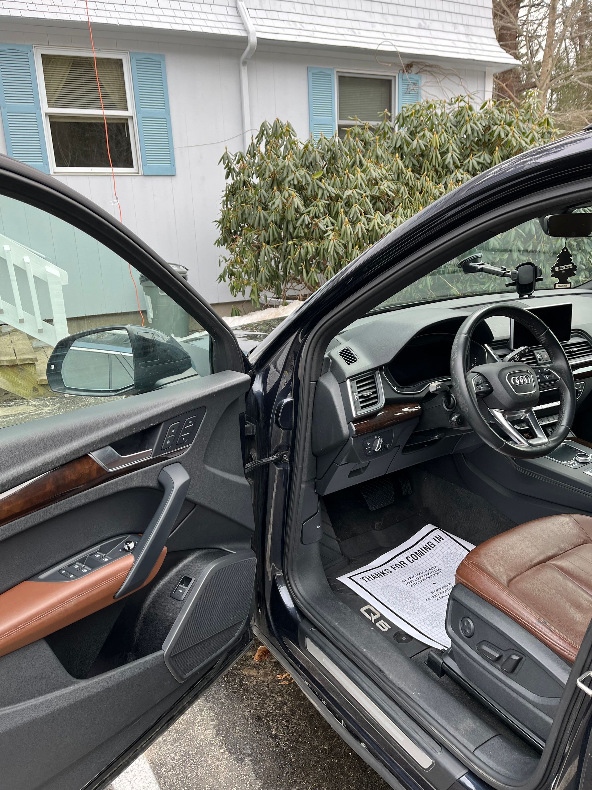 Car with open doors showing a brown-and-black interior parked in a driveway outside a house.