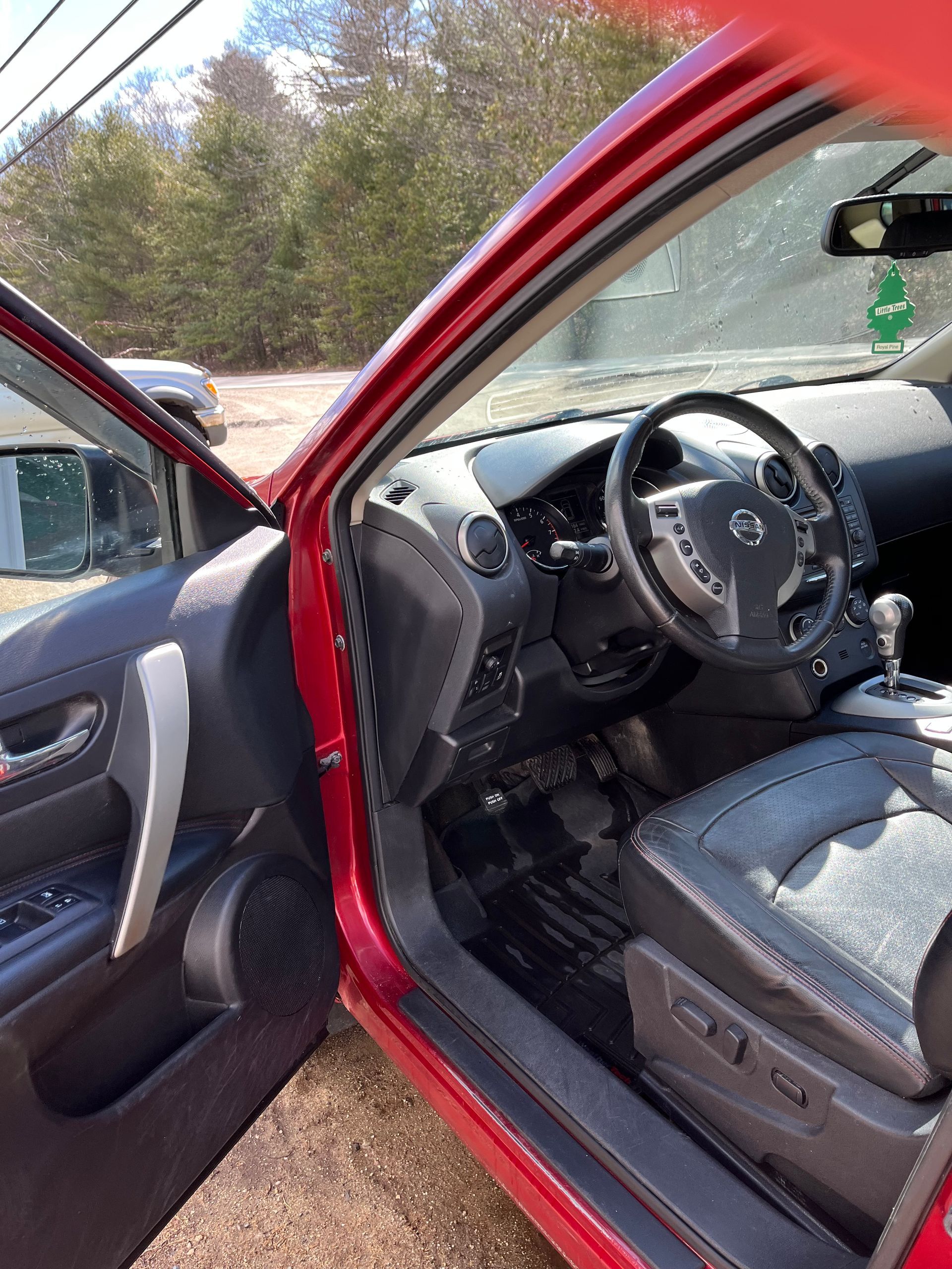 Open red car door showing gray interior and steering wheel in daylight