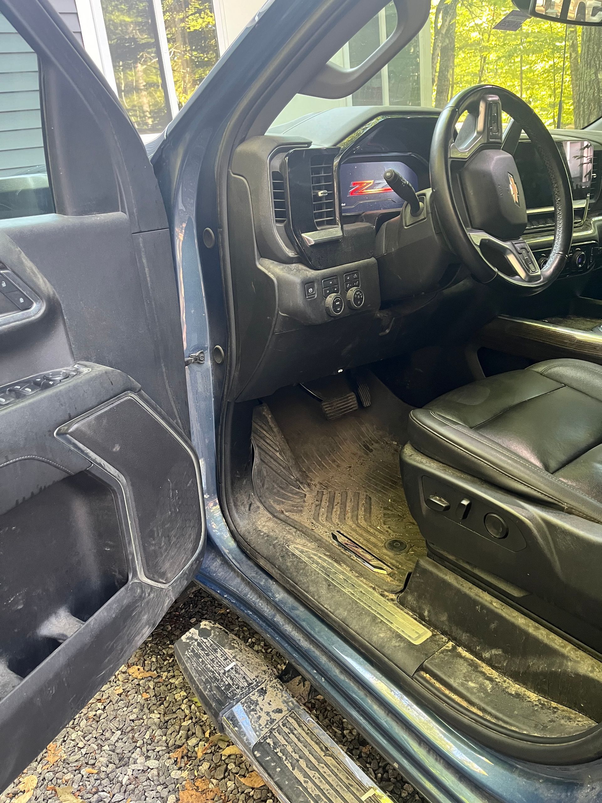 Open car door view of a black vehicle interior with steering wheel, dashboard, and muddy floor mats.