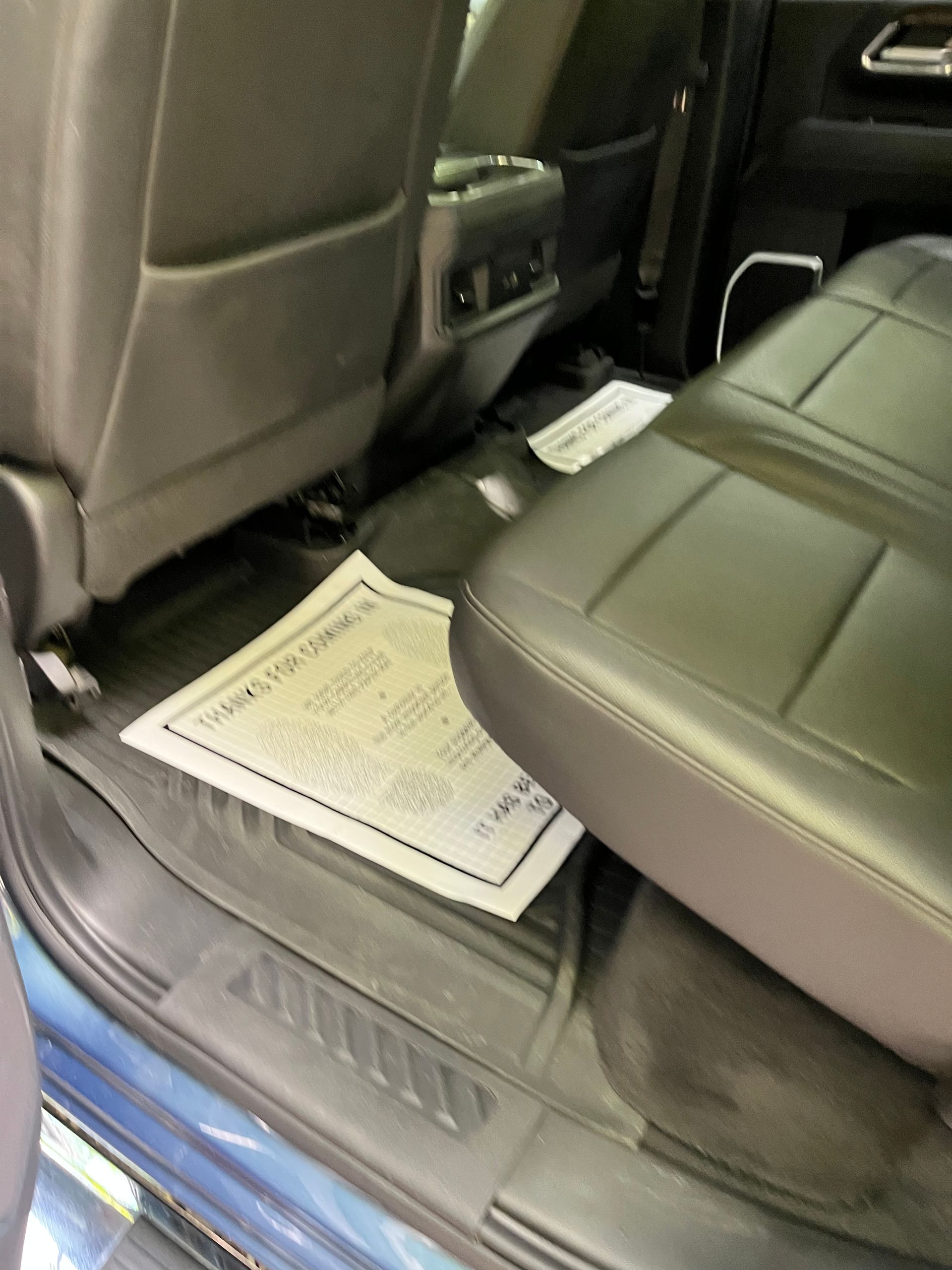 Rear car seat with a floor mat, black leather seats, and a paper floor cover on the floor