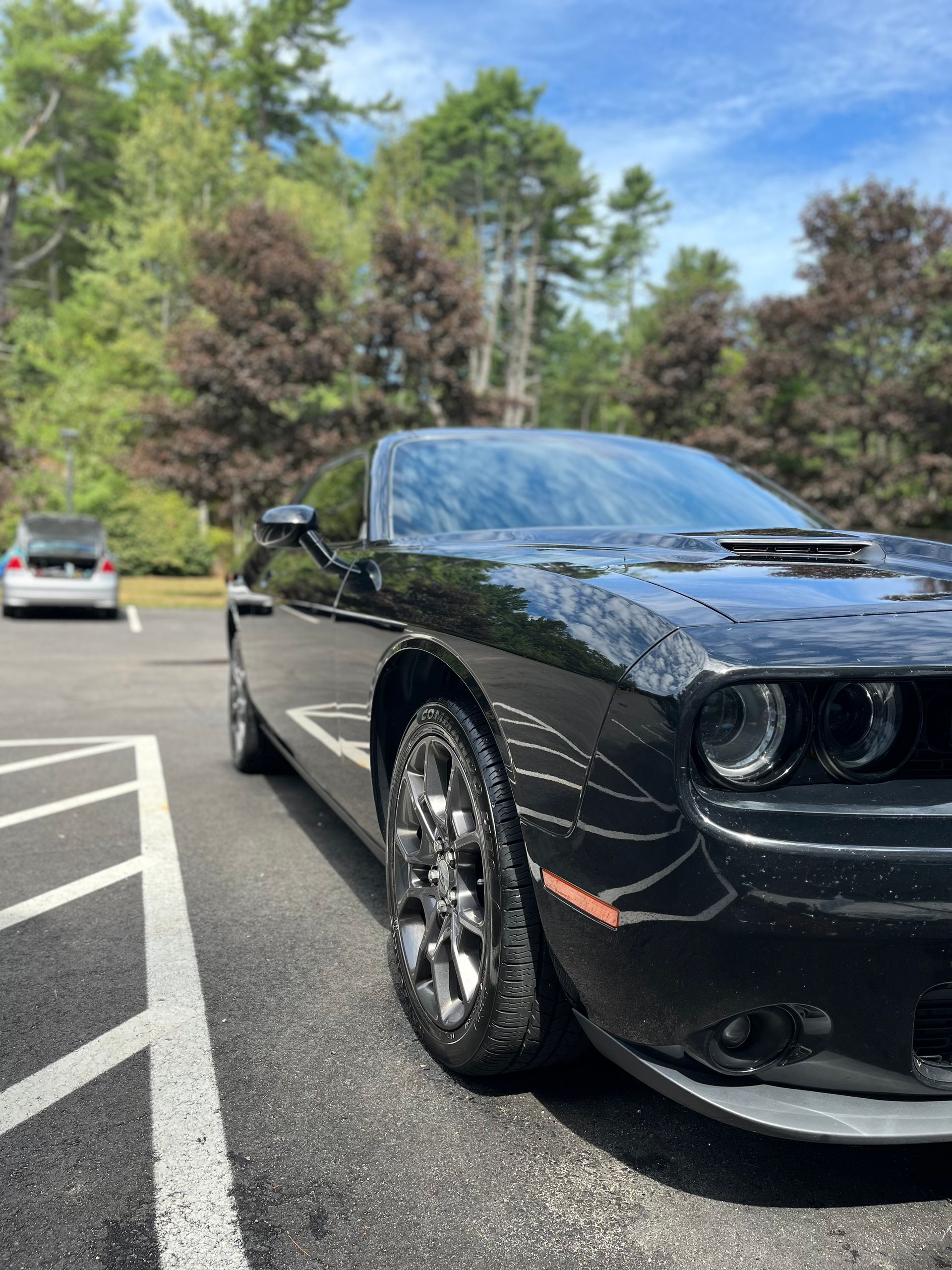 Black sports car parked in a lot under trees, front view with shiny chrome wheels