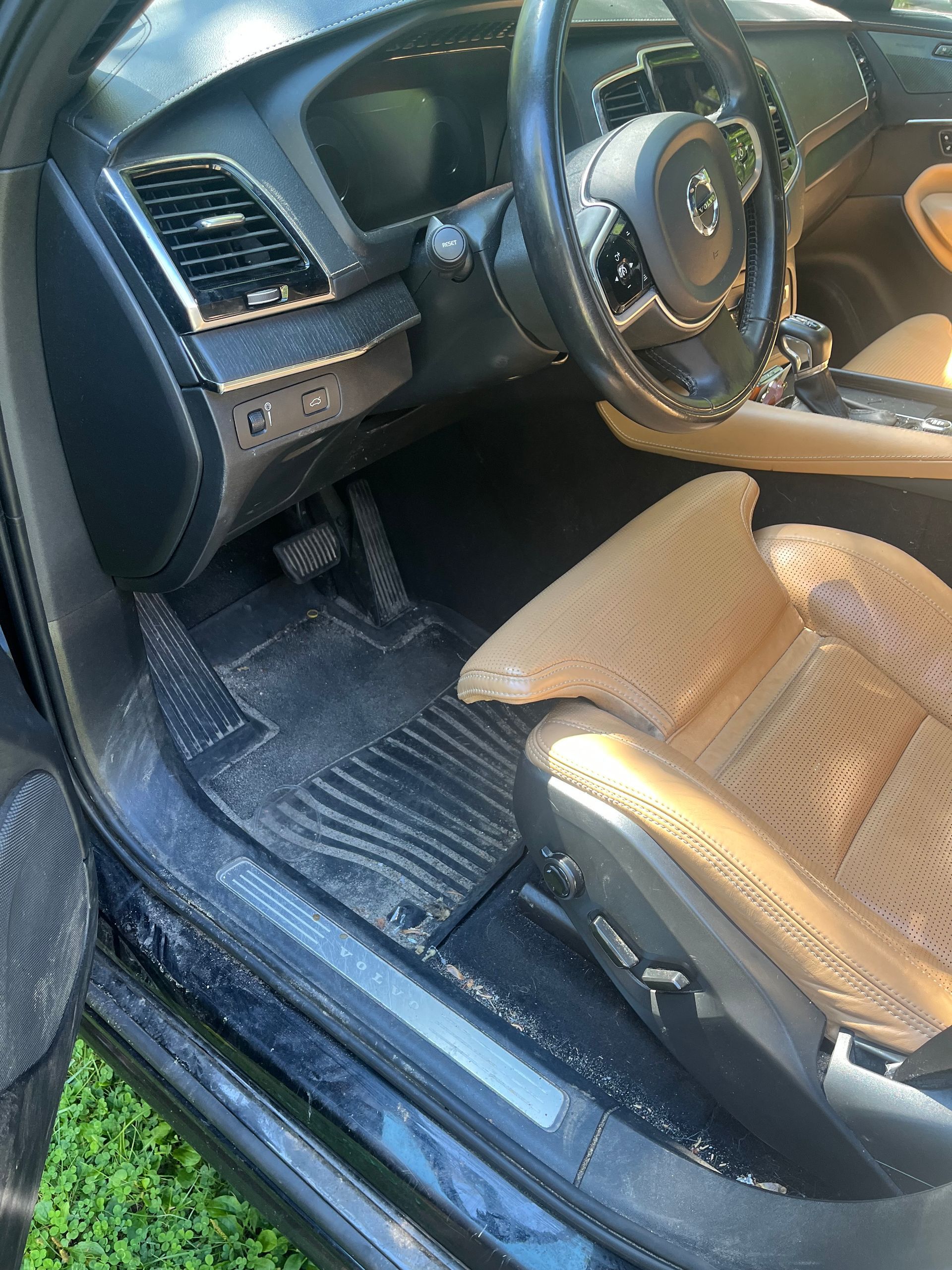 Car interior with black dashboard, steering wheel, and tan seat cover on the driver’s seat.