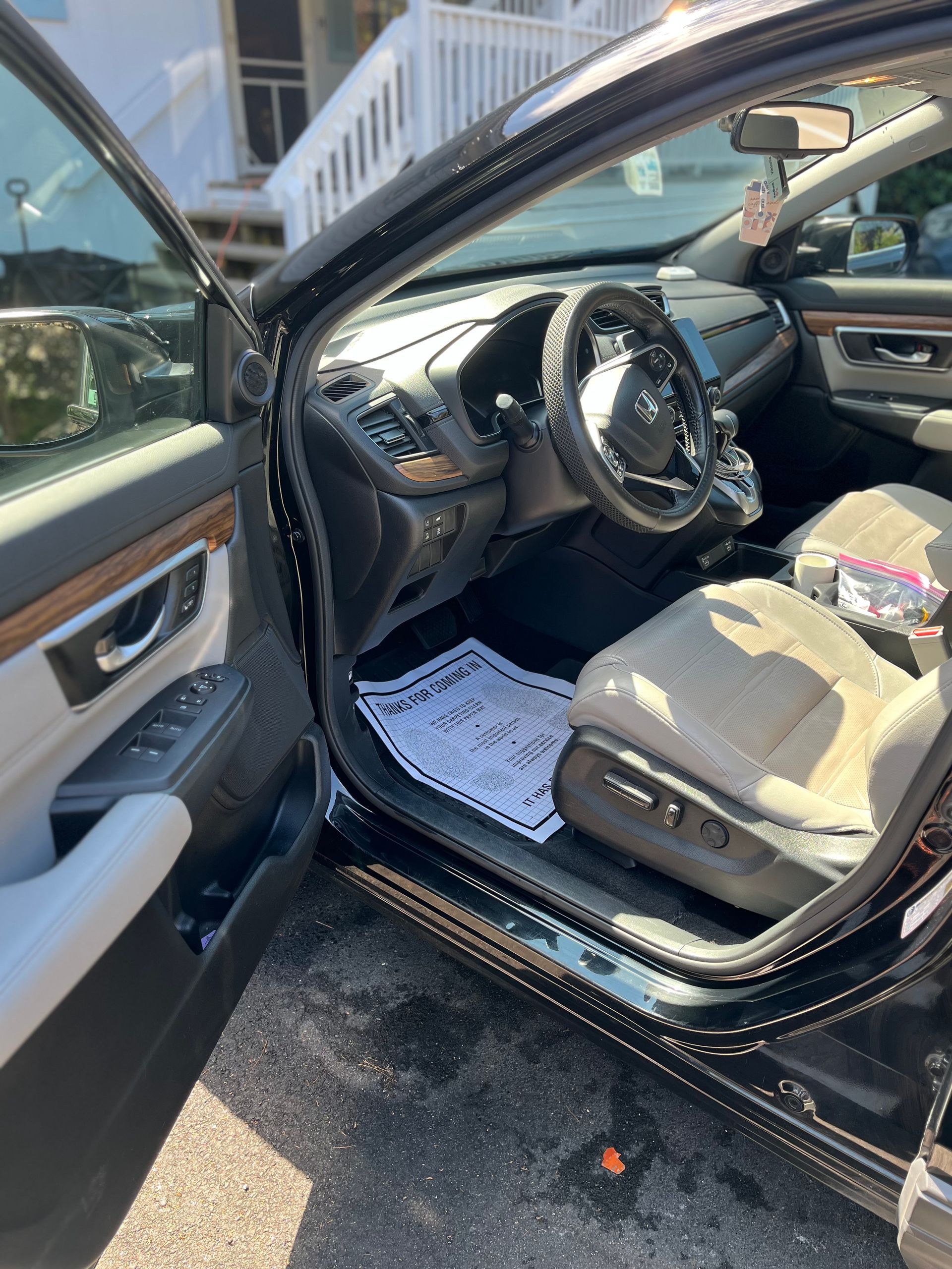 Open driver’s side door of a black car, showing the beige interior and steering wheel.