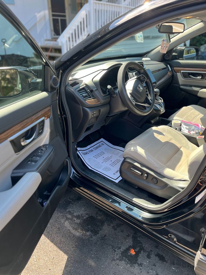 Open driver’s side door of a black car, showing the beige interior and steering wheel.