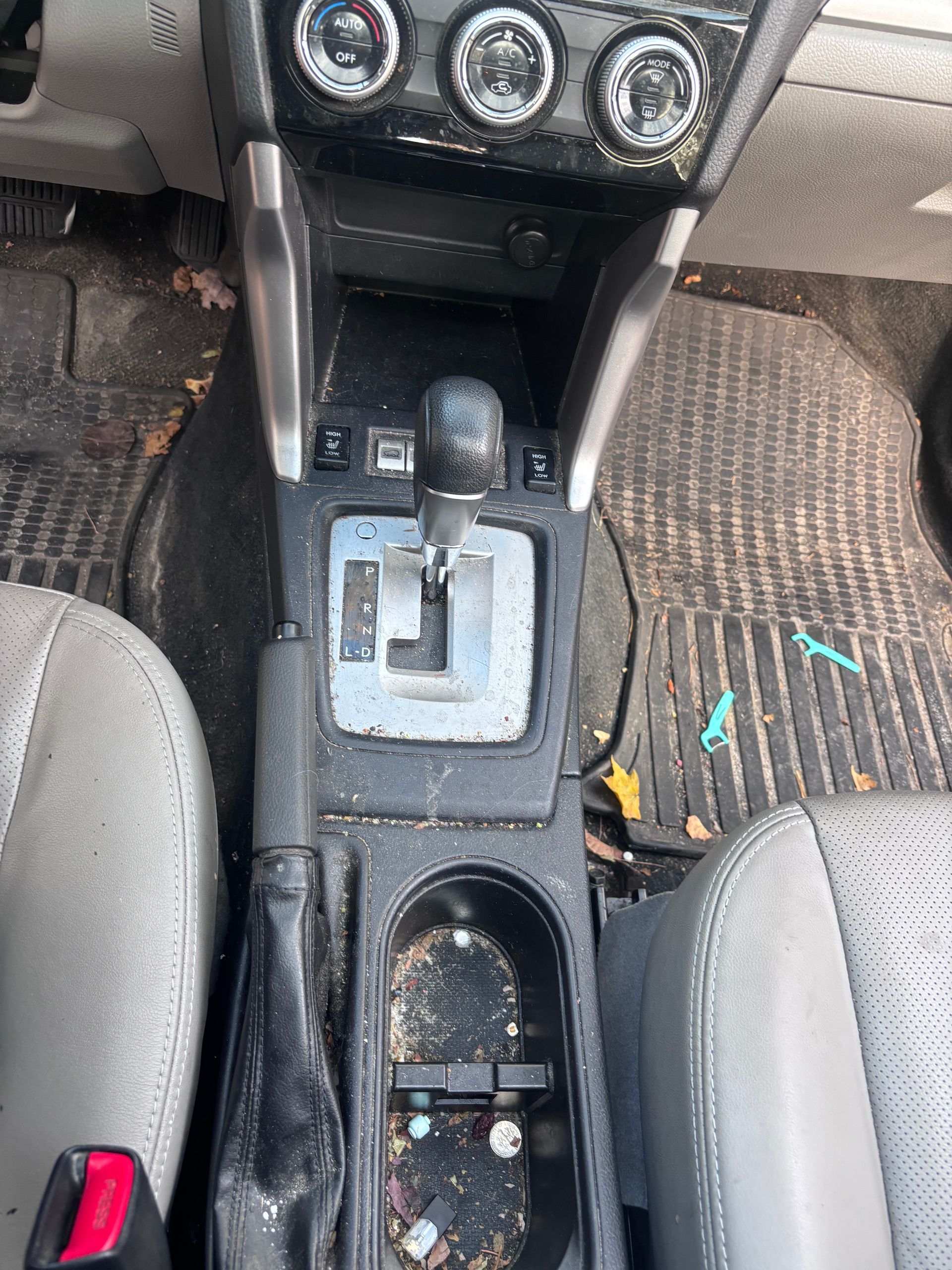 Car interior center console with gear shifter, cup holders, and a dirty floor mat with debris.