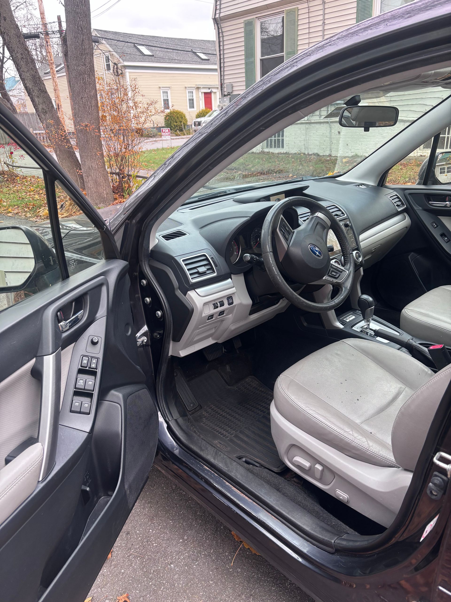 Open car door showing a gray interior and steering wheel, parked outside a house.