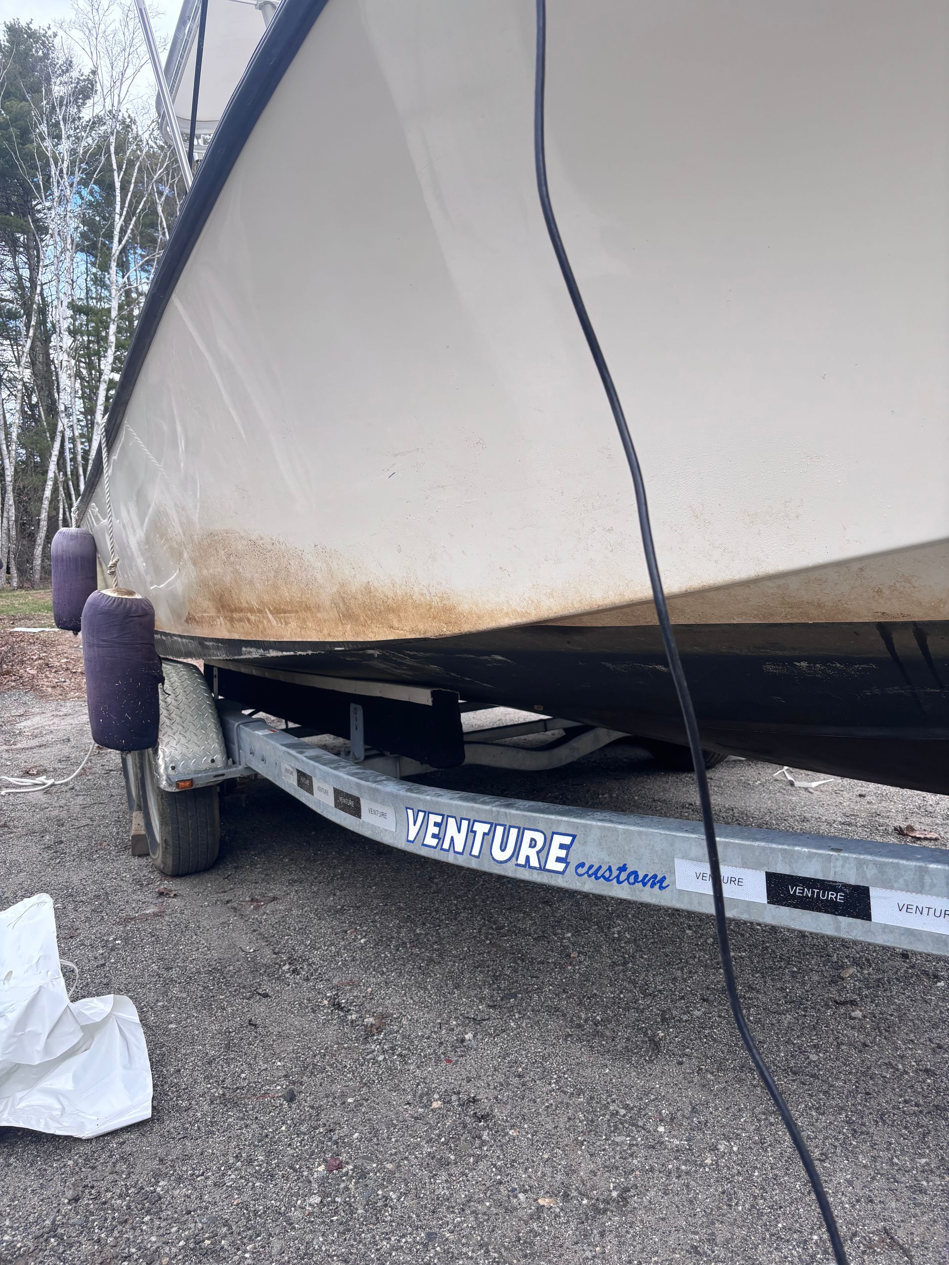 Tarp-covered sailboat on gravel, showing hull side and trailer supports outdoors.