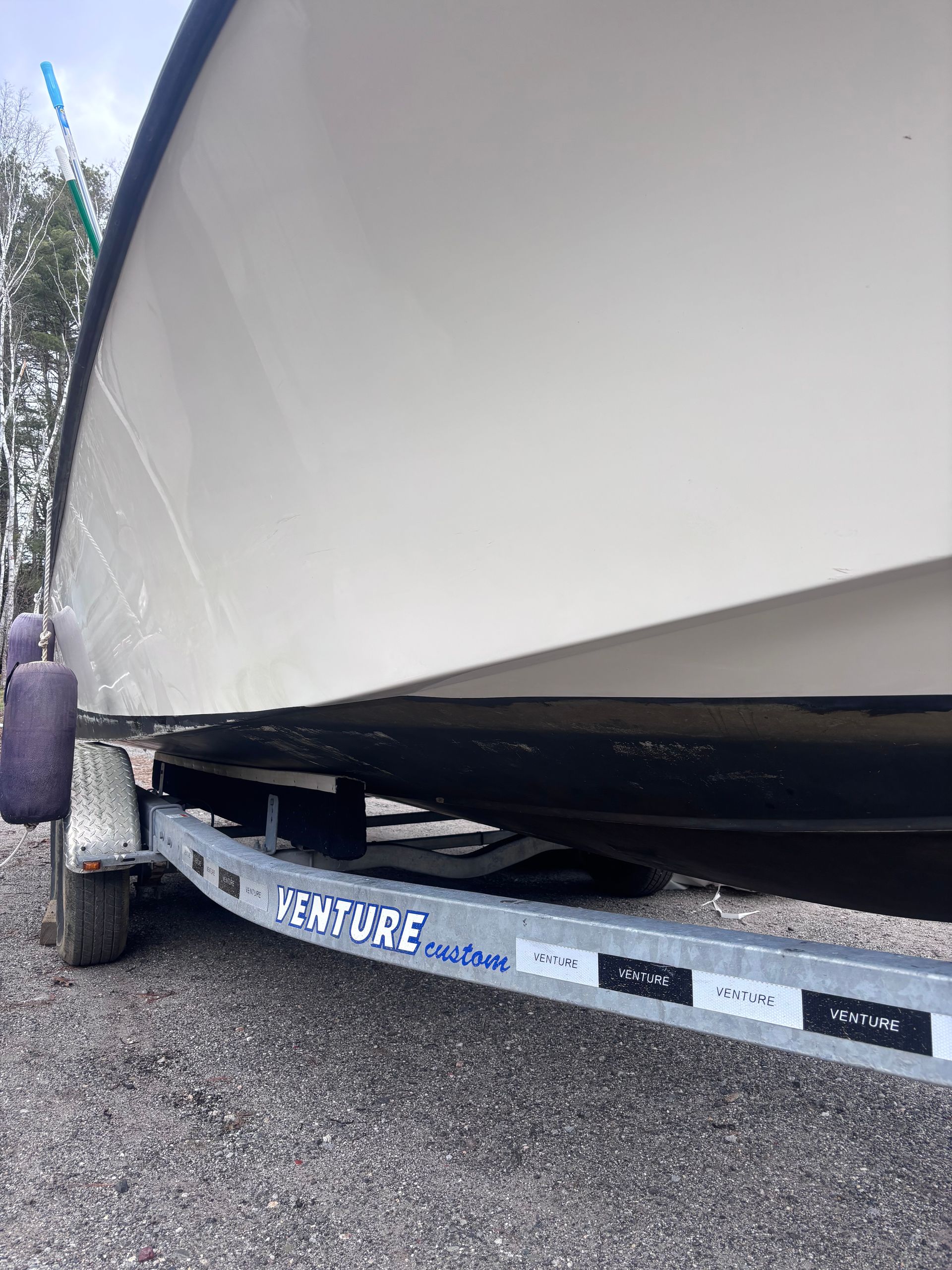 White boat hull on a trailer over gravel, close-up side view