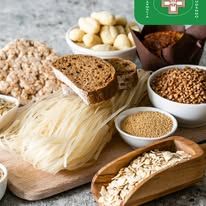 Una superficie di legno espone vari tipi di cereali, pane, pasta e prodotti da forno, a rappresentare diversi carboidrati.