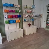 In un negozio con pavimento effetto legno, si vedono due scaffali bianchi pieni di vari prodotti di bellezza e per la cura della persona.