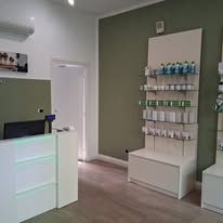 Un moderno interno d'ufficio caratterizzato da un bancone reception bianco, pareti verde oliva e una scaffalatura che espone diversi prodotti.