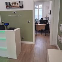 Una moderna area reception con scrivania bianca, pareti verde oliva, pavimento effetto legno e una porta aperta che conduce a un ufficio.