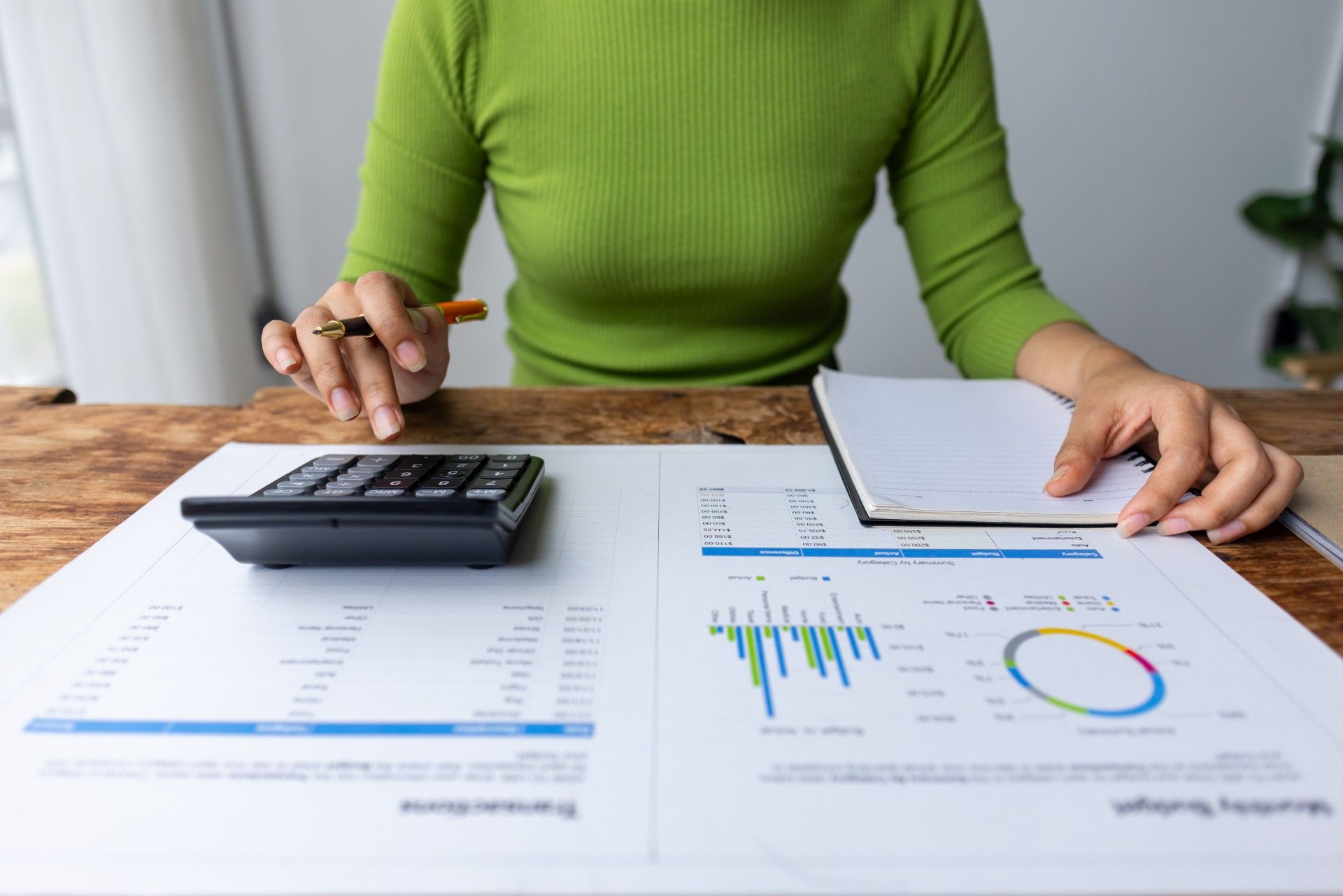 A woman is sitting at a table with a calculator and a notebook.