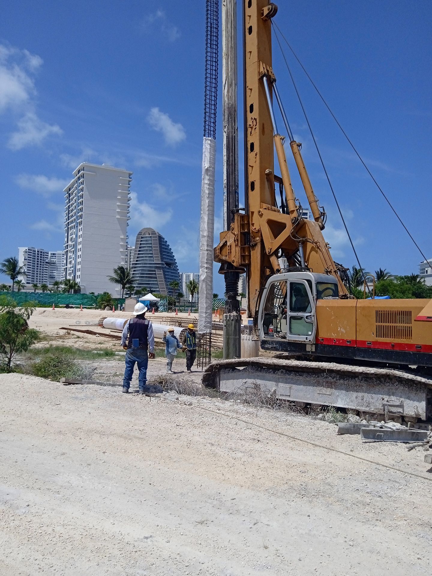 Un grupo de trabajadores de la construcción está parado frente a una gran excavadora amarilla.