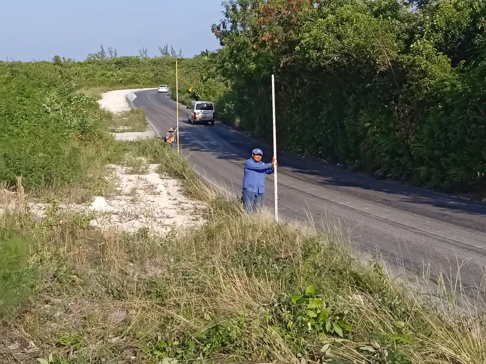 Un hombre parado al costado de una carretera sosteniendo un poste.