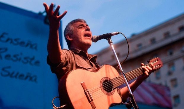 Un hombre cantando en un micrófono mientras sostiene una guitarra.