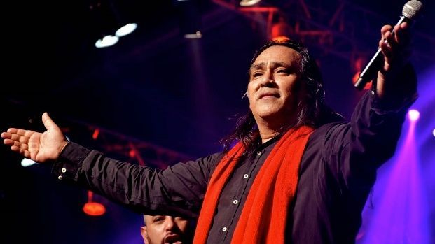 Un hombre con una bufanda roja está cantando con un micrófono en un escenario.