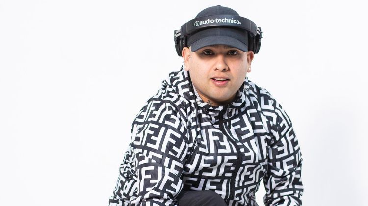 Un hombre que lleva auriculares y un sombrero está de pie delante de un fondo blanco.