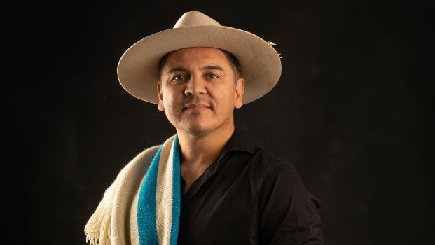 Un hombre que lleva un sombrero y una bufanda está de pie delante de un fondo negro.