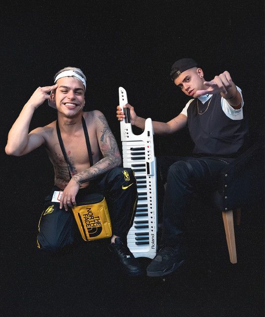 Un hombre sin camisa está sentado junto a un hombre que sostiene un teclado.