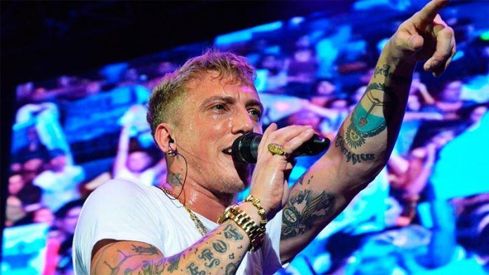 Un hombre con tatuajes está cantando en un micrófono frente a una multitud.