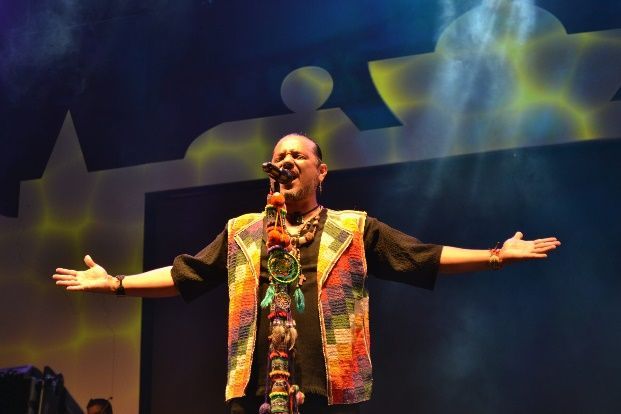 Un hombre cantando en un micrófono con los brazos extendidos.