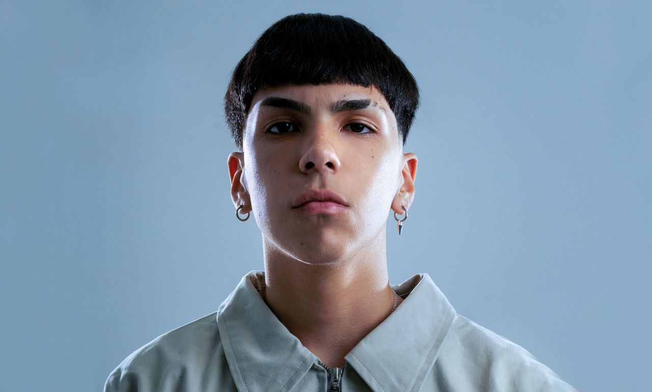 Un joven que lleva una chaqueta y pendientes mira a la cámara.
