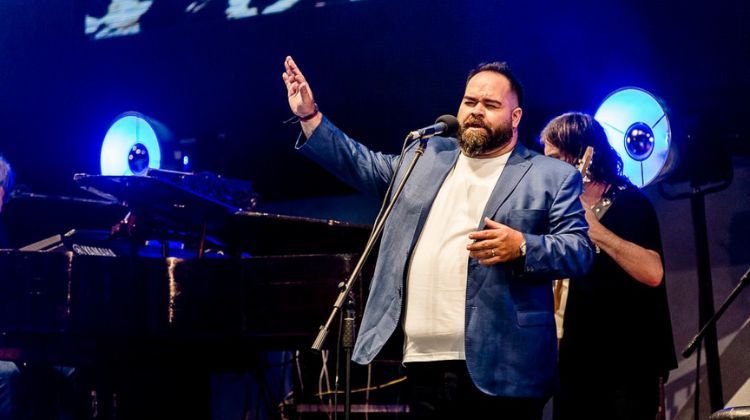 Un hombre con un traje azul está cantando con un micrófono en un escenario.