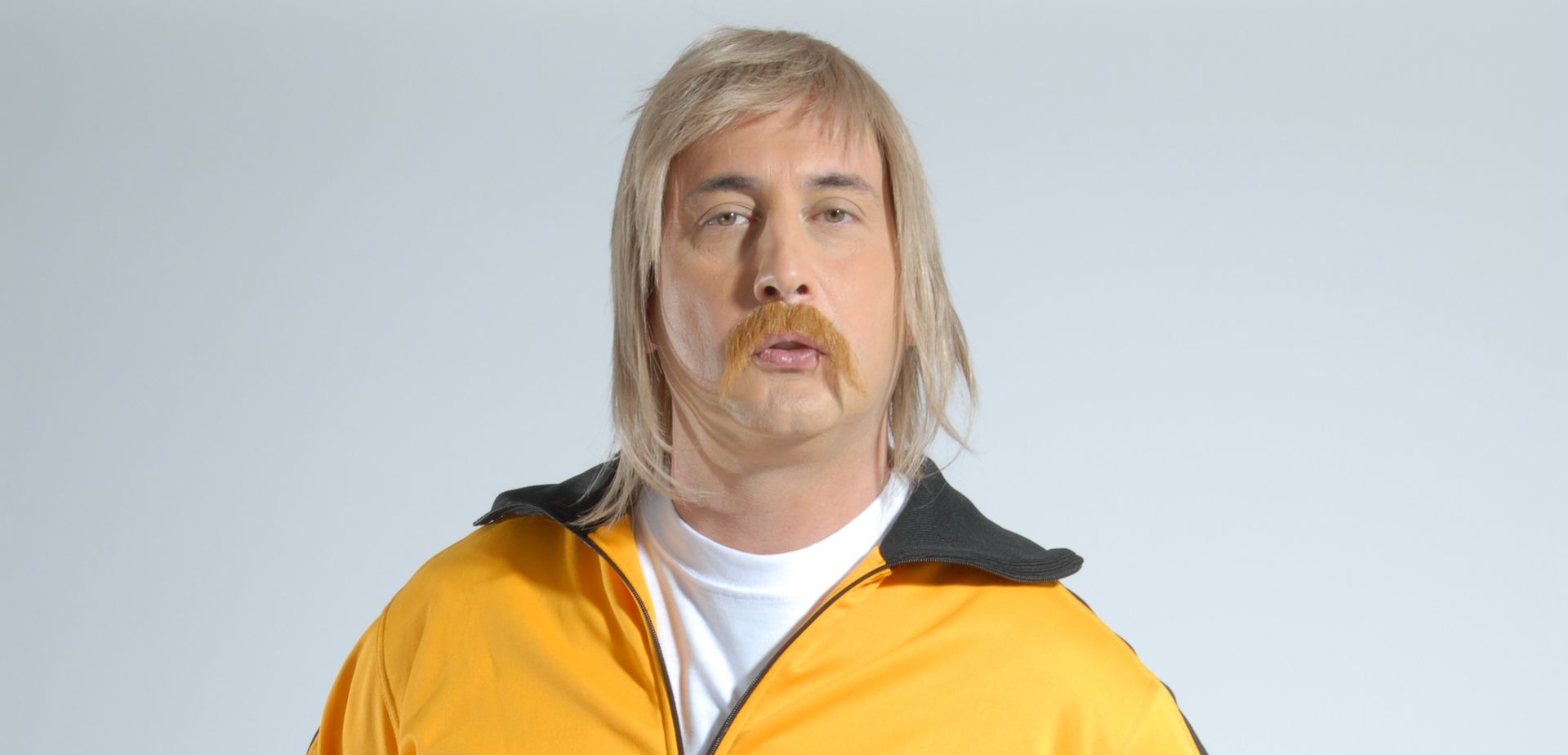 Un hombre con cabello rubio y bigote lleva una chaqueta amarilla.