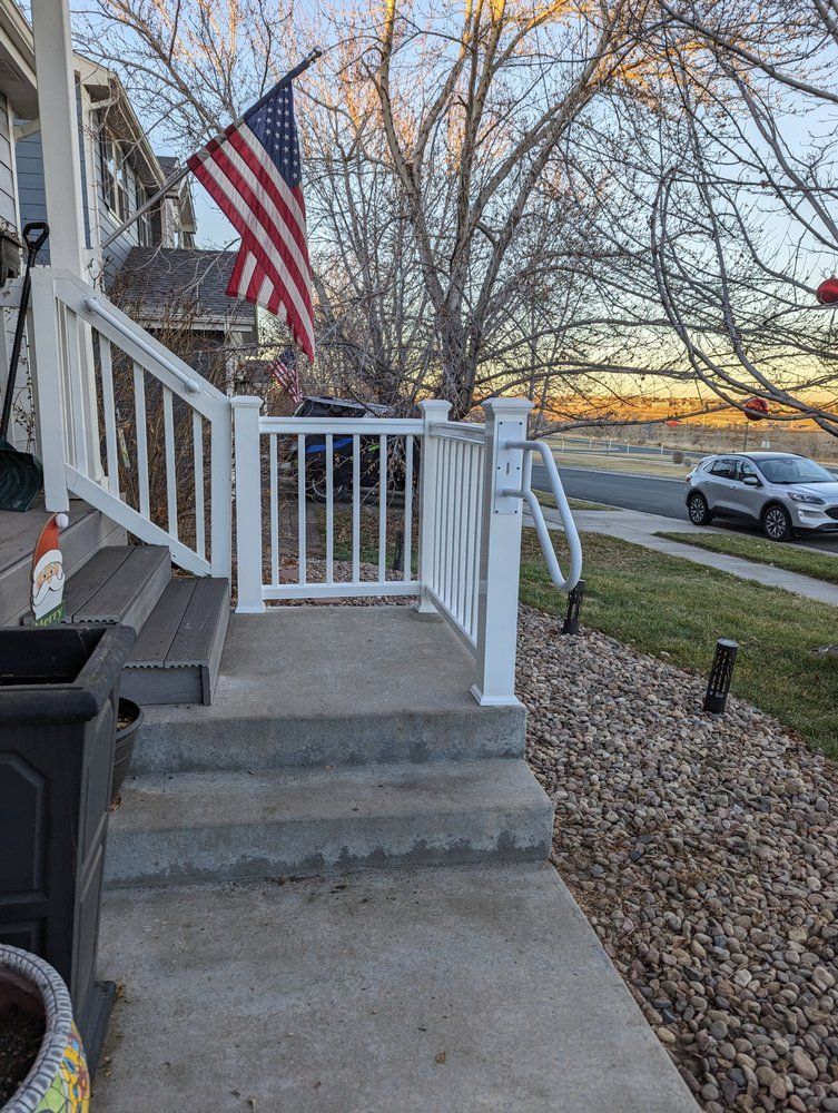 Front porch with white railing, concrete steps, American flag, and gravel landscaping.