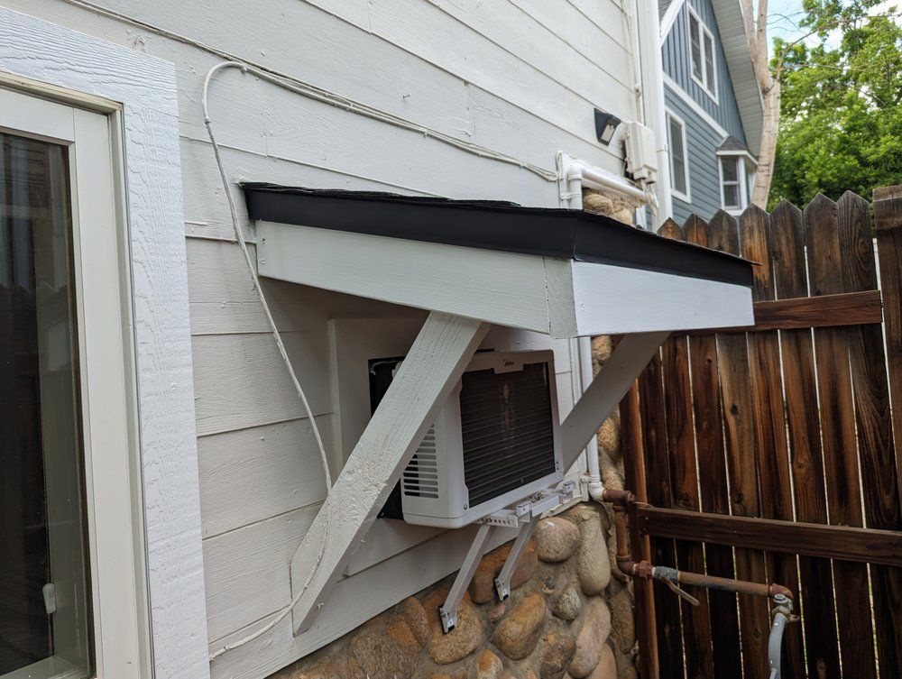 White air conditioner mounted in a wall, under a white and black wooden awning.