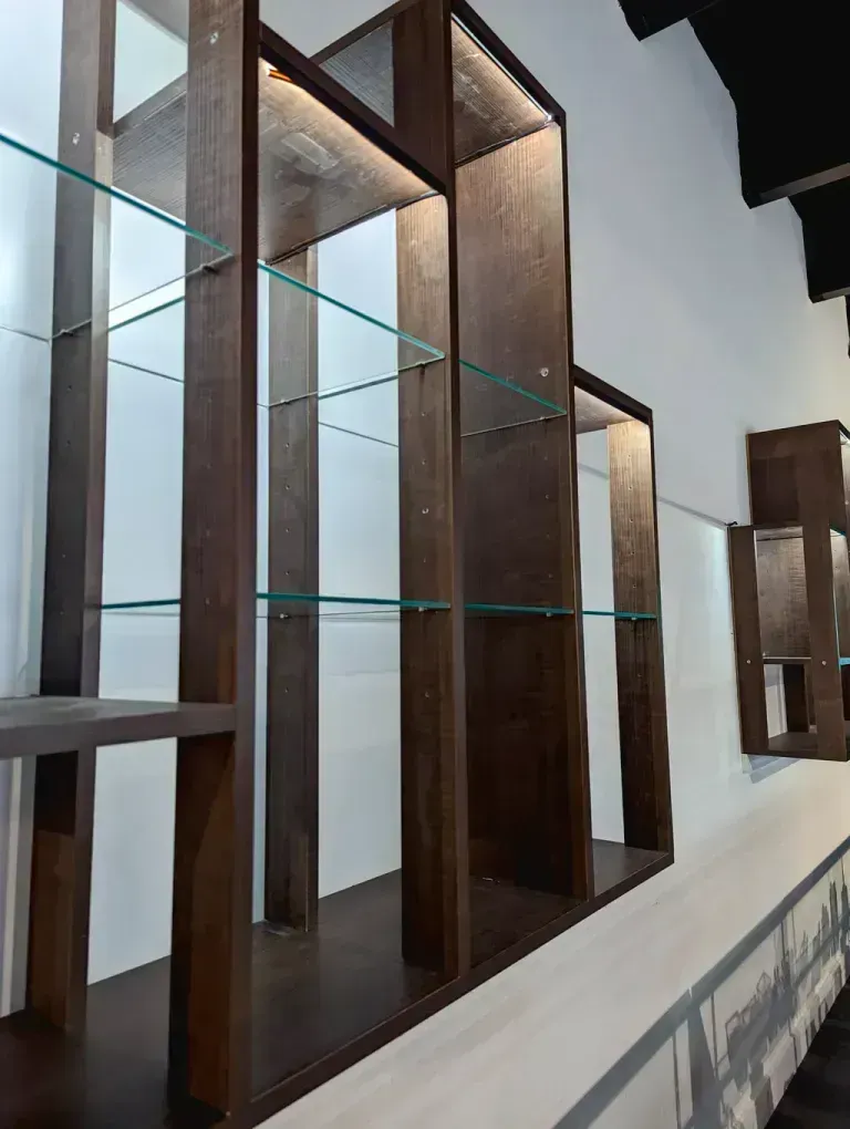 Wooden display shelves with glass shelves against a white wall.