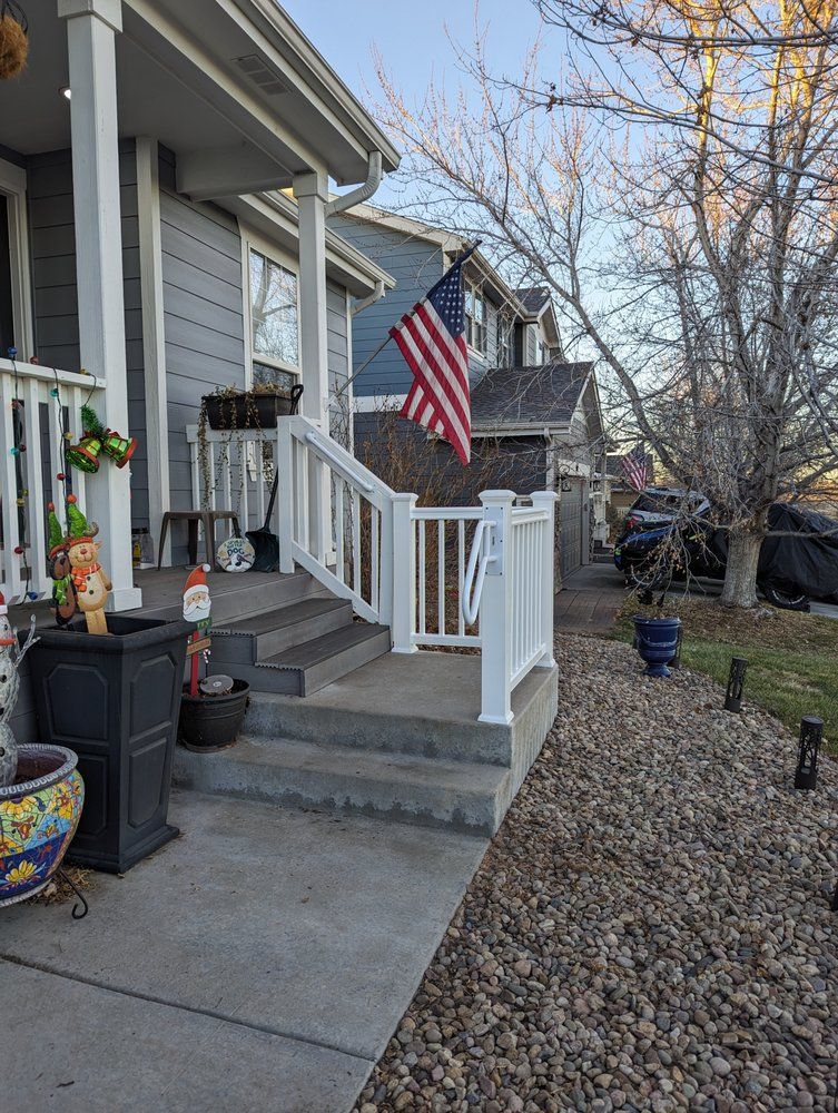 A porch with an American flag, steps, and a white railing in front of a gray house.