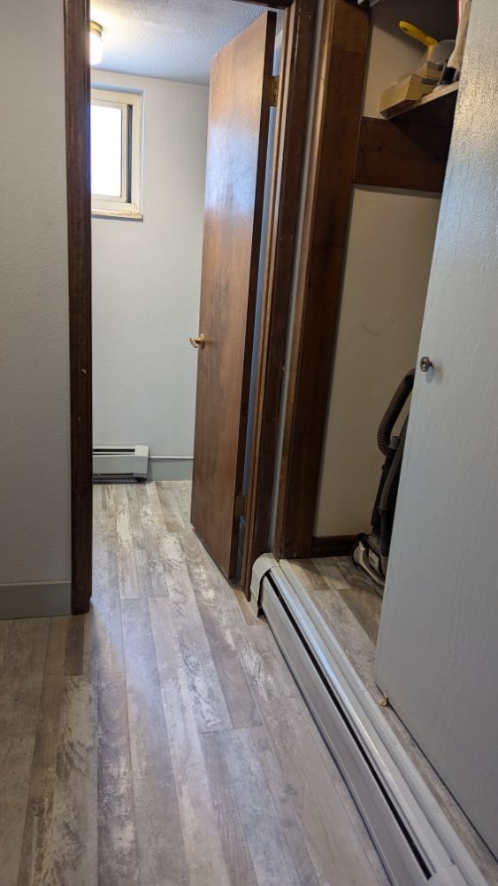 Narrow hallway with wood-look flooring, leading to a door. A closed closet and a radiator are on the right.