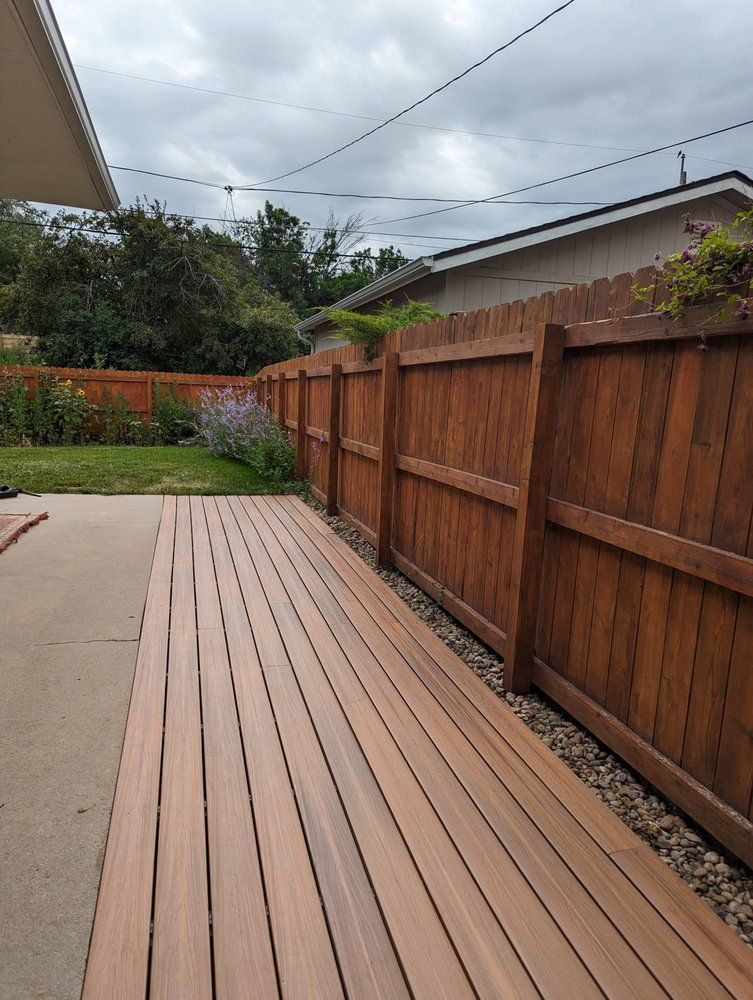 Wooden deck and brown fence along a backyard, under a cloudy sky.
