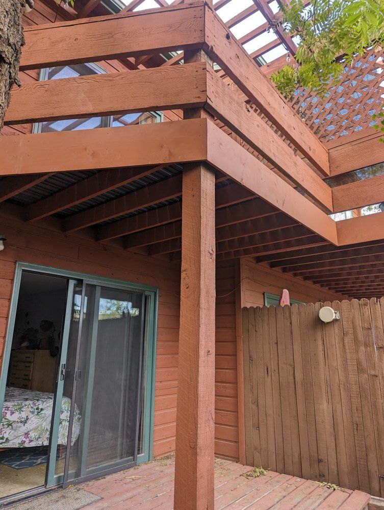 Wooden deck with railing, supported by a post, overlooking a yard and sliding glass door.