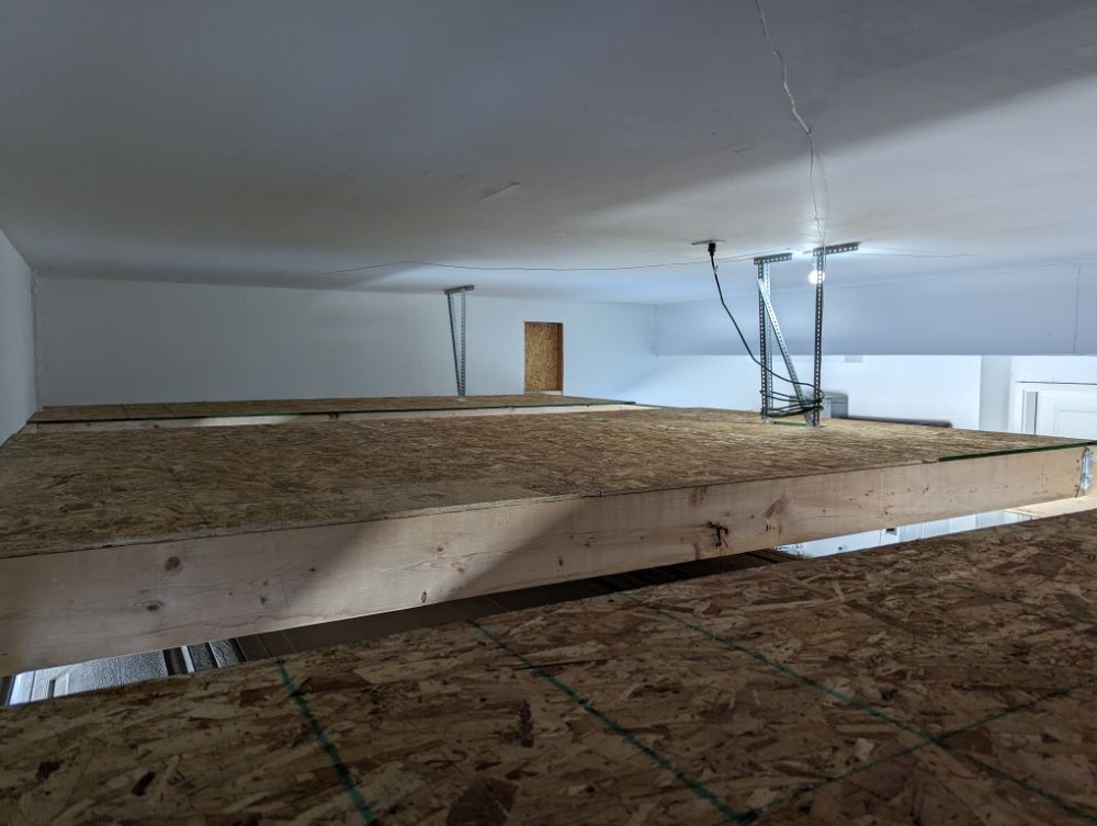 Interior view of unfinished loft space with exposed wooden beams and plywood flooring.