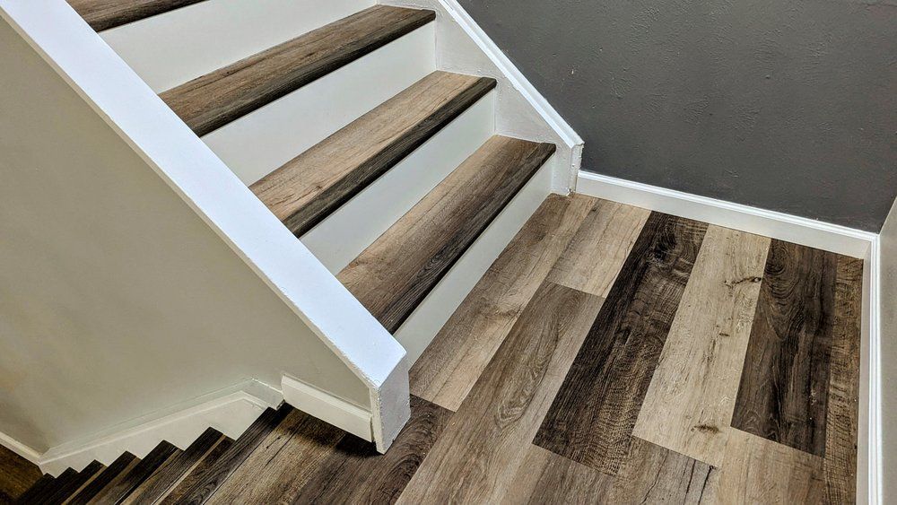 Staircase with wood-look steps and flooring. White trim on the sides. Grey wall in the background.