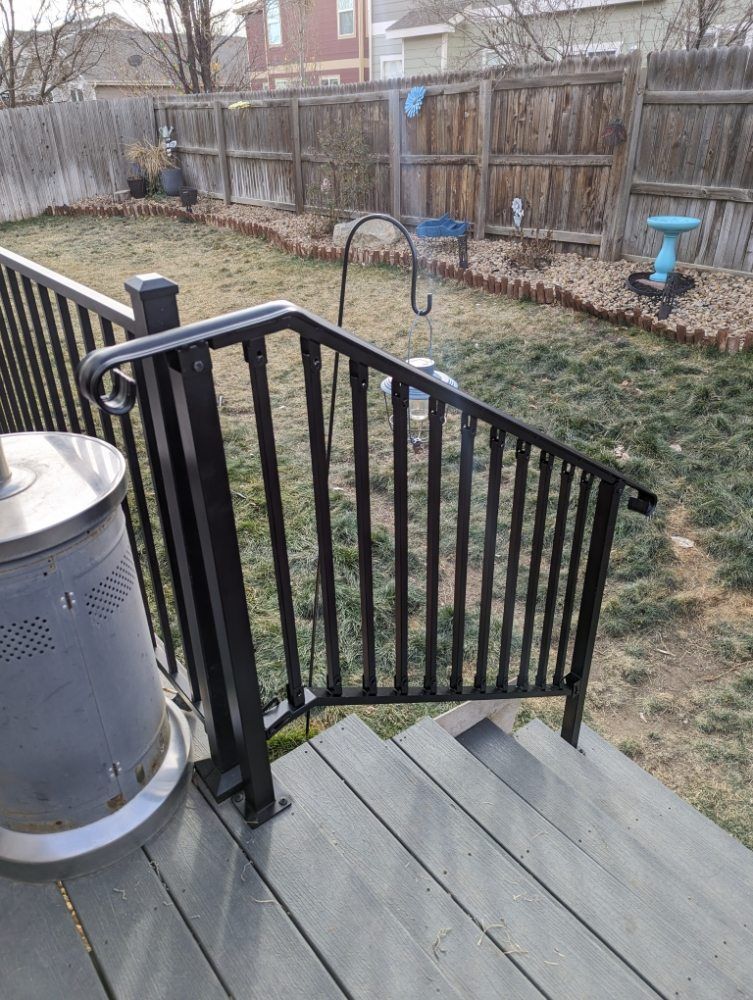 Black metal handrail on outdoor deck with steps, looking out to a backyard with fence, and a patio heater.