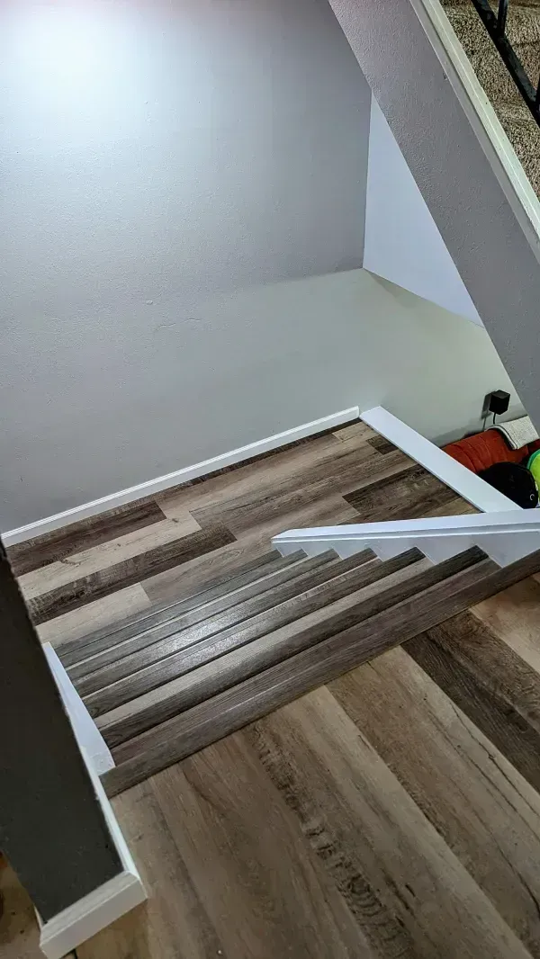 Wood-look flooring installed on a staircase with white trim, against gray and white walls.