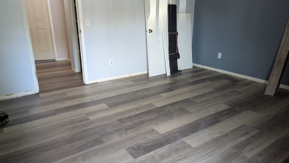 Room with wood-look flooring and gray and white walls. A doorway leads to another room.