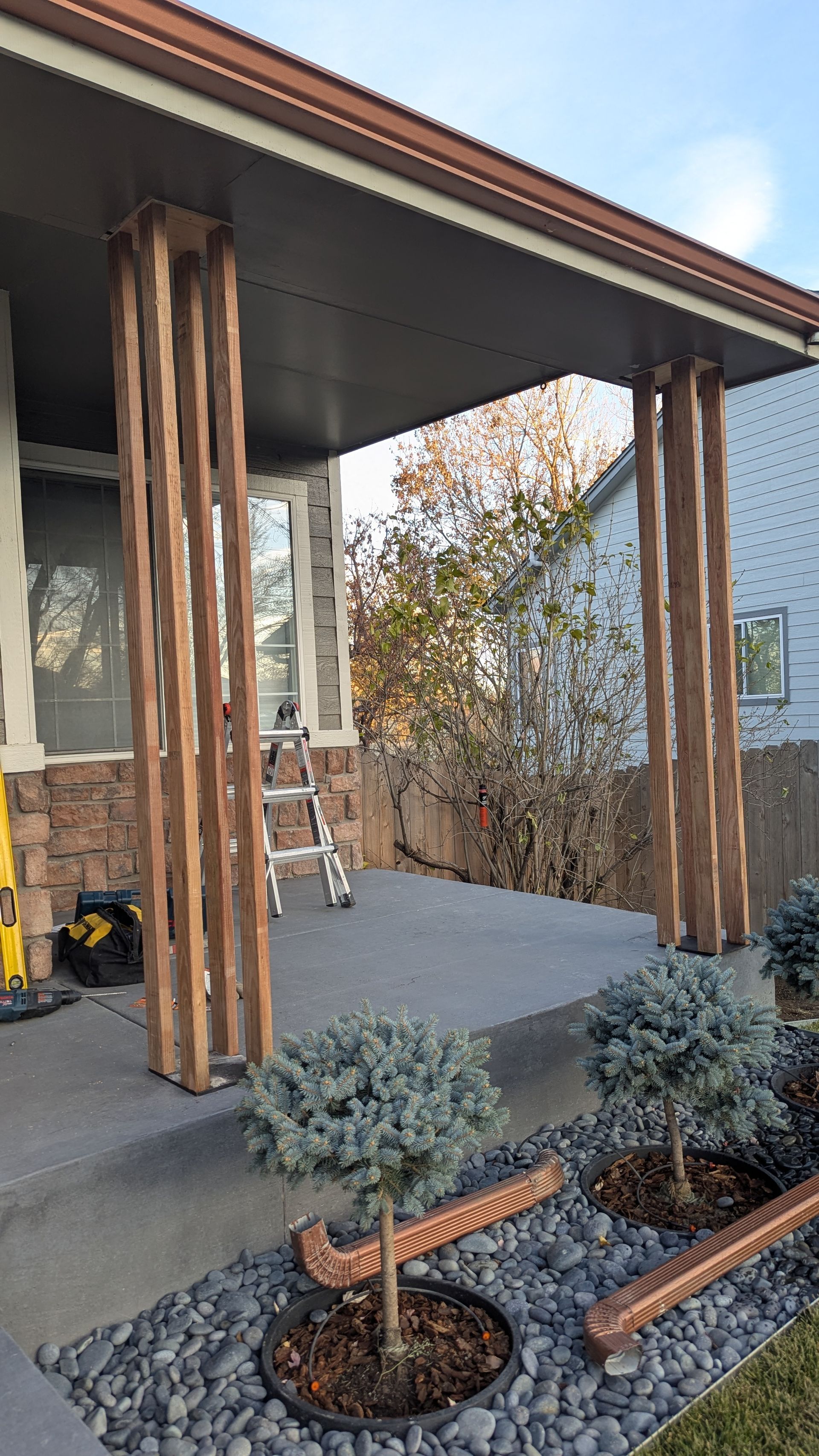 Porch with brown wooden columns, gray concrete floor, and small blue-green bushes.