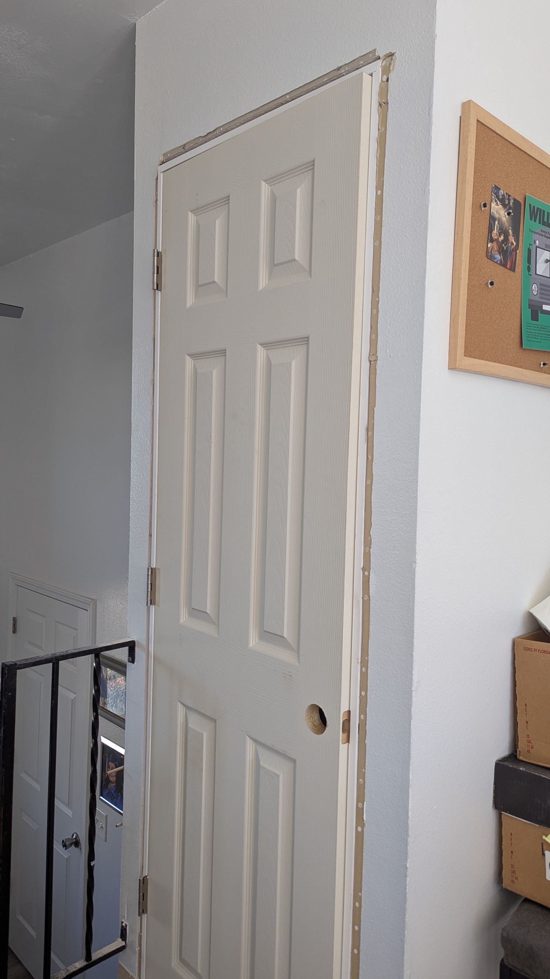 White six-panel door with doorframe and corkboard on the right. A railing and shoe organizer are on the left.