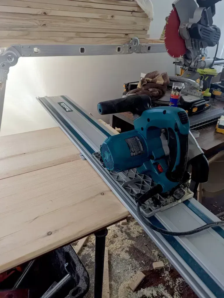 A blue circular saw on a track is cutting wood on a workbench indoors.