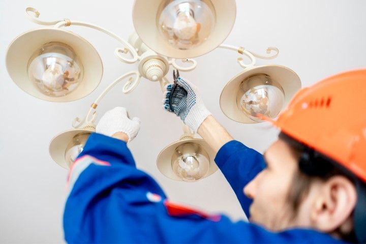 Electrician in orange hard hat replacing lightbulb in chandelier.
