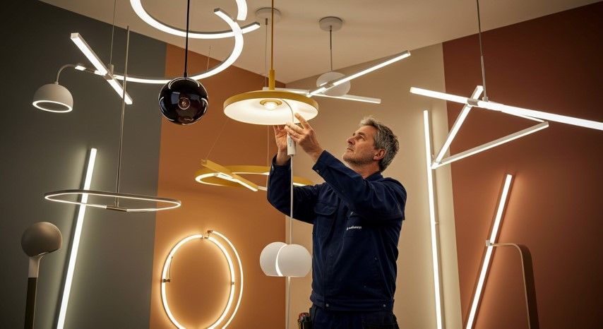 Man adjusting a yellow pendant lamp surrounded by various modern light fixtures.
